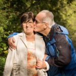 Older couple walking in a park man is kissing her on the cheek and she is smiling