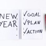 Notebook with grid paper with the words "New Year' written on one side and "Goal, Plan, Action" with checkmarks on the other side with pen lying next to it